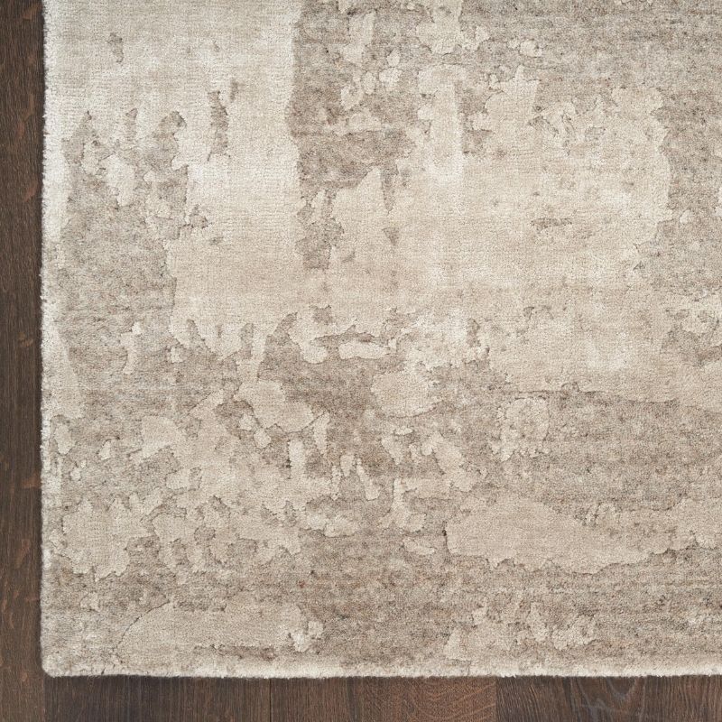 A close-up of a distressed area rug with a mottled beige and taupe pattern, shown on a dark brown wooden floor.