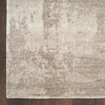 A close-up of a distressed area rug with a mottled beige and taupe pattern, shown on a dark brown wooden floor.