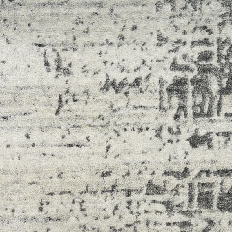A close-up of a textured area rug with a distressed, faded traditional pattern in charcoal gray and off-white.