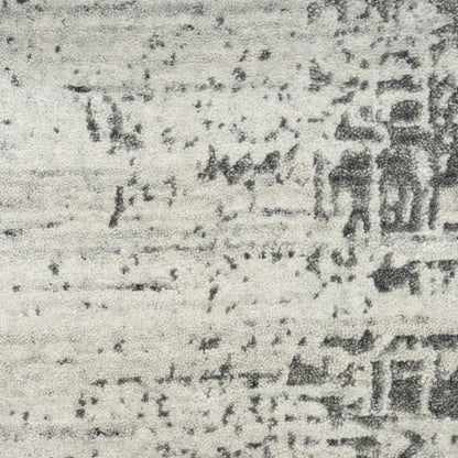 A close-up of a textured area rug with a distressed, faded traditional pattern in charcoal gray and off-white.