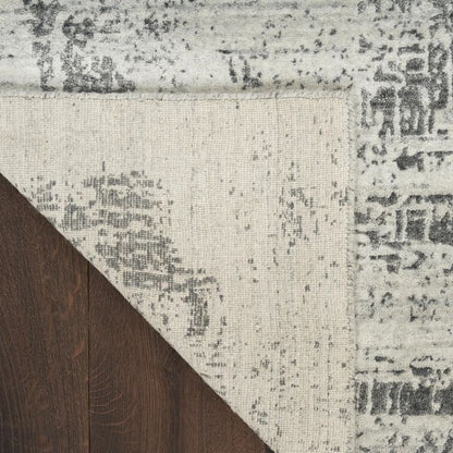Close-up of a distressed area rug corner showing a cream and gray pattern with a dark brown wood floor visible underneath.