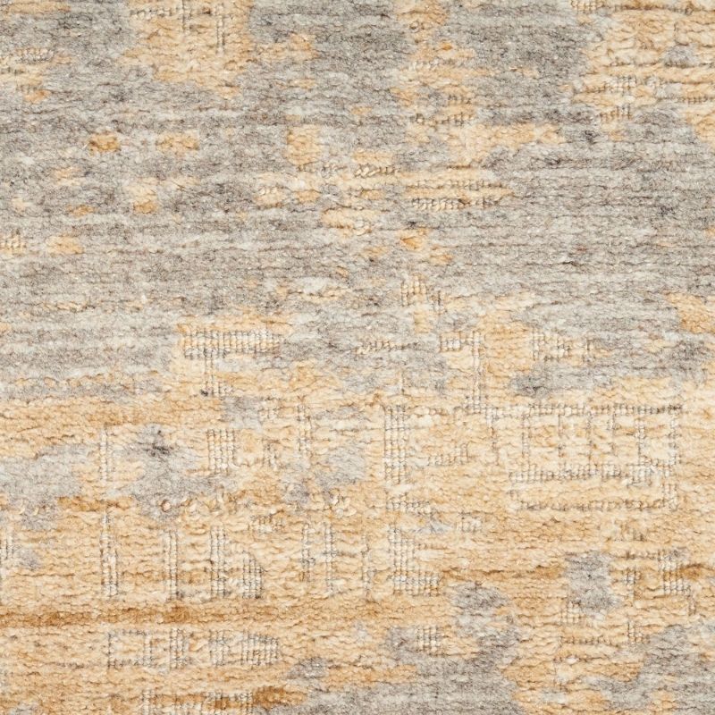 A close-up of a textured area rug with a distressed, abstract pattern in warm beige, tan, and light gray.