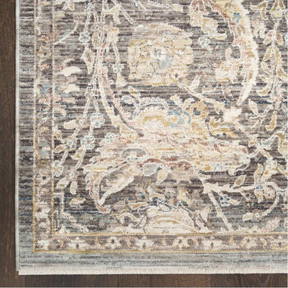 A close-up of a distressed traditional area rug with an ornate floral and vine pattern in muted beige, gray, brown, and soft blue tones, laid over a dark wood floor.