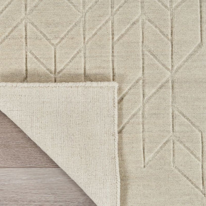 Close-up of a light beige textured rug with a geometric diamond pattern, showing the underside and folded corner over a light wood floor.
