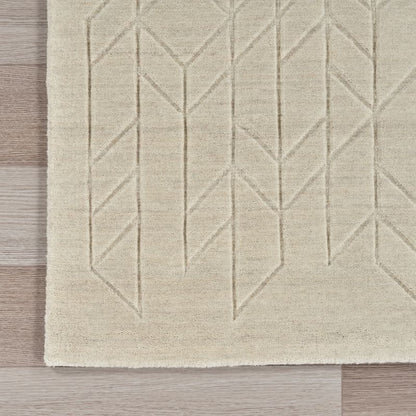 A close-up of a light beige area rug with a geometric, raised chevron-like pattern, shown on a light wood floor.