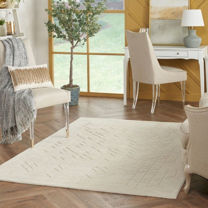 An off-white rectangular area rug with a subtle geometric pattern, styled in a bright, modern living room with wood floors, beige chairs, and a window.