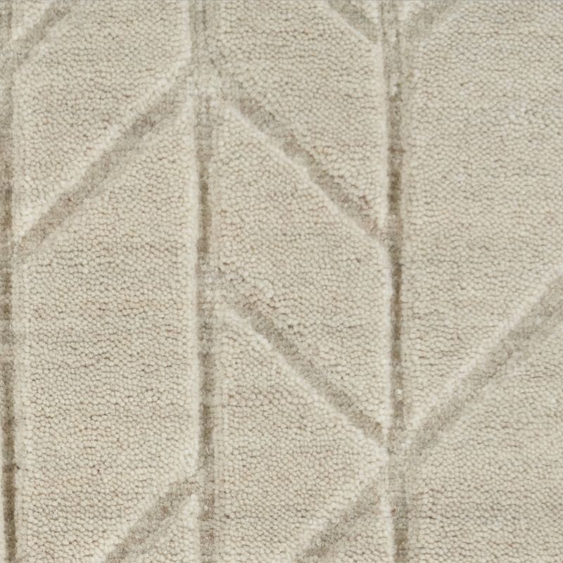 A close-up of a textured fabric or carpet in a warm off-white/cream tone with a subtle geometric pattern formed by slightly raised lines.