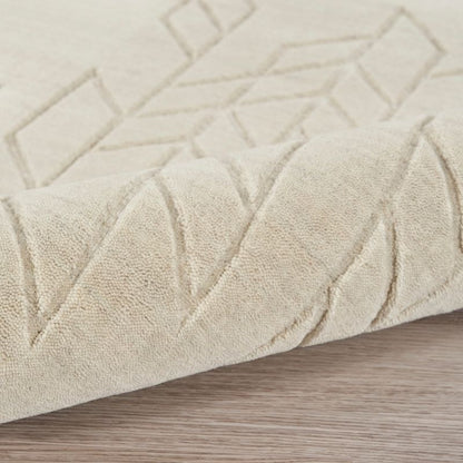 A close-up of a light beige textured rug with a geometric diamond pattern, shown folded over to reveal its pile and texture on a light wood floor.