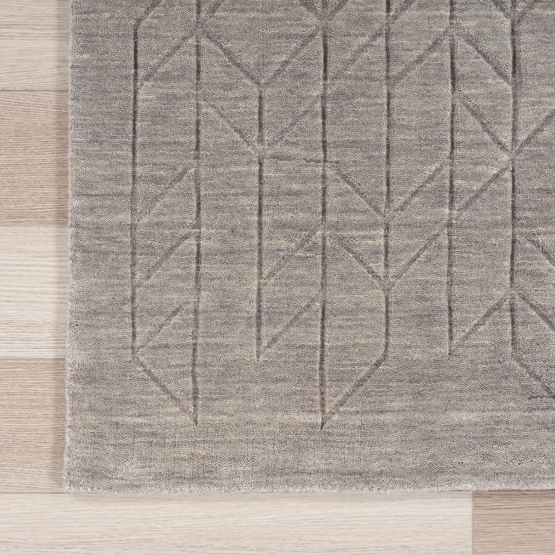 A close-up of a gray textured area rug with a geometric pattern, laid out on a light-colored wooden floor.