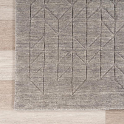 A close-up of a gray textured area rug with a geometric pattern, laid out on a light-colored wooden floor.