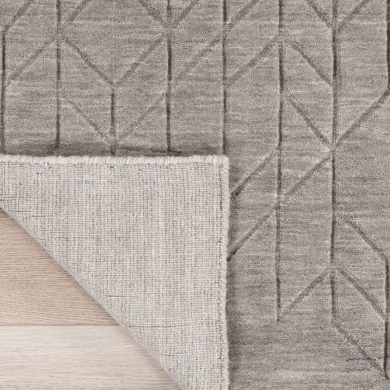 Close-up of a gray textured area rug with a geometric raised pattern, showing the pile from the top and the woven underside, laid over a light wood floor.
