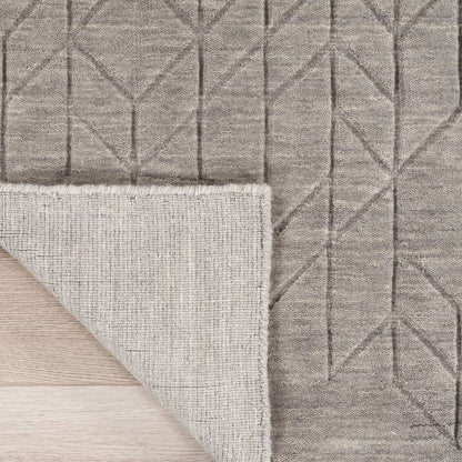 Close-up of a gray textured area rug with a geometric raised pattern, showing the pile from the top and the woven underside, laid over a light wood floor.