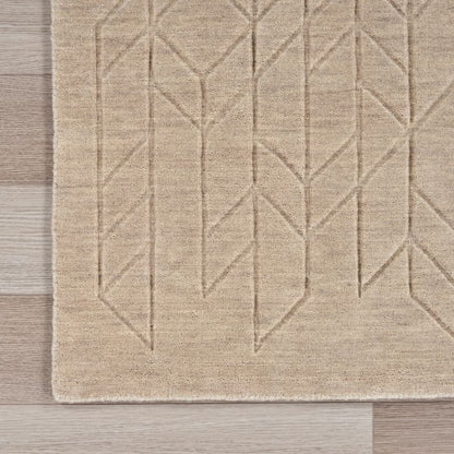 A close-up of a beige area rug with a geometric, raised chevron-like pattern, laid out on a light wood floor.