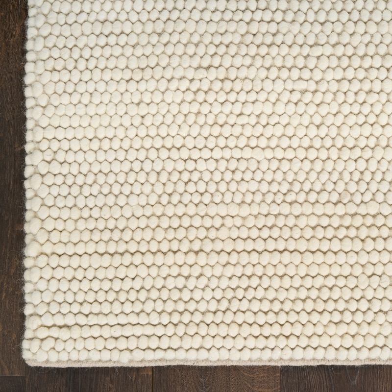 A close-up of a cream-colored textured area rug with a raised honeycomb pattern, shown on a dark brown wooden floor.