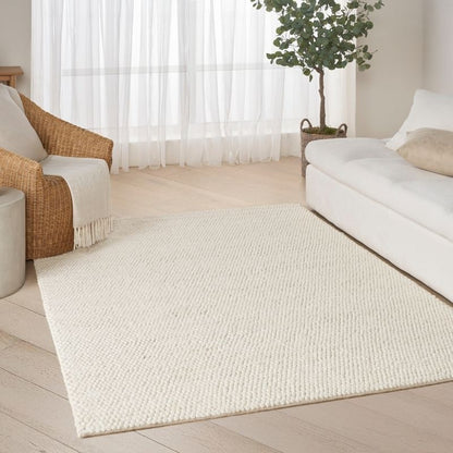 Living room with a white rug, white sofa, and wicker chair.
