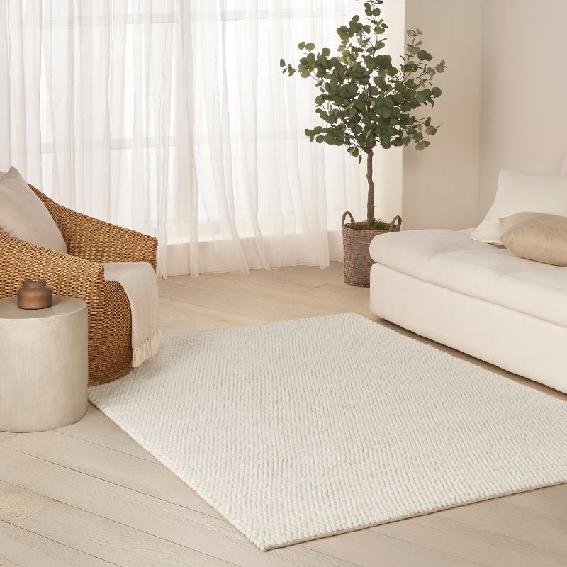 Living room with a white rug, beige sofa, wicker chair, and potted plant.