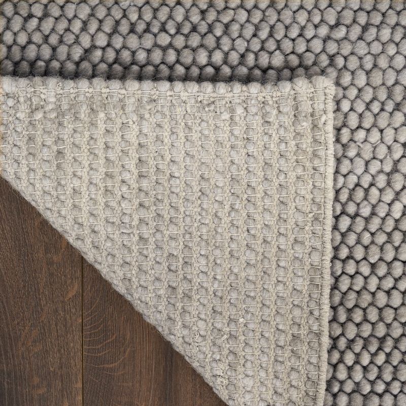 Close-up of a textured gray rug corner on a wooden floor.