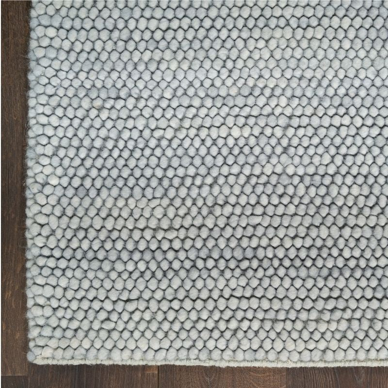 A close-up of a textured area rug with a repeating hexagonal pattern in light gray and off-white, shown on a dark wood floor.