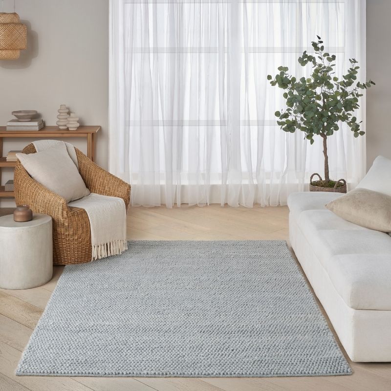 Living room with a gray rug, wicker chair, white sofa, and plant.
