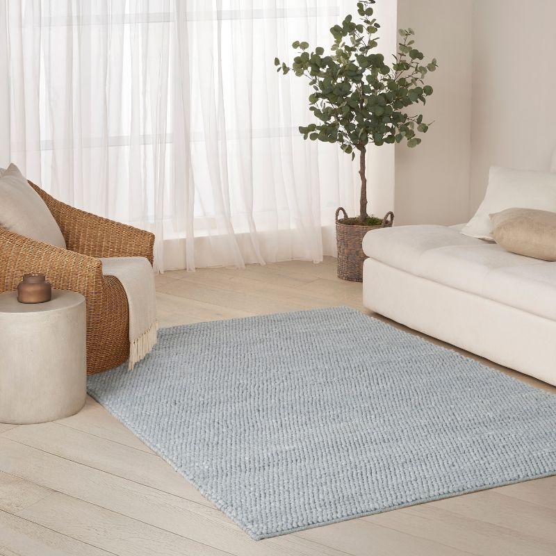 Living room with a light blue rug, wicker chair, and white sofa.