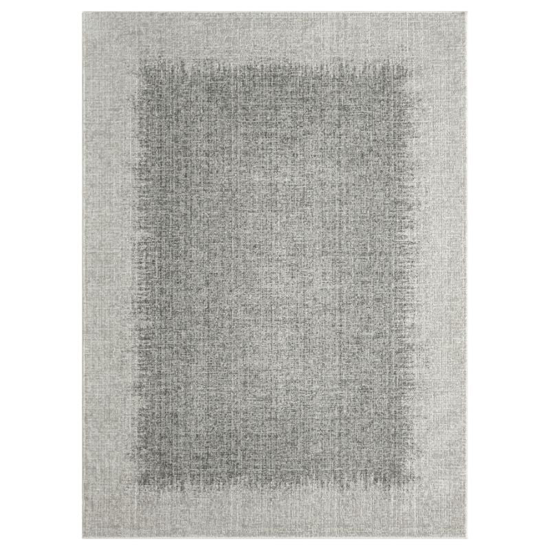 A rectangular area rug with a textured, distressed pattern in shades of gray, featuring a darker gray central panel surrounded by a lighter gray border.