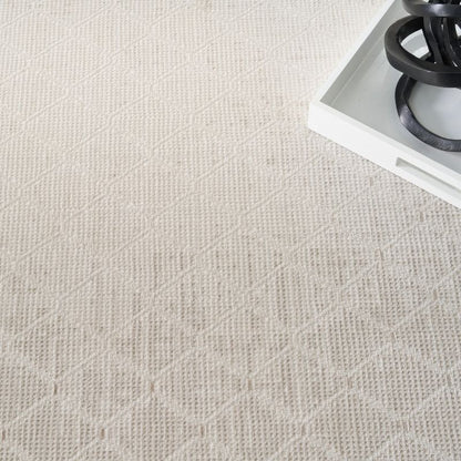 A close-up of a light beige textured rug with a subtle geometric diamond pattern, shown with a white tray and black decorative rings in the top right corner.