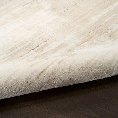 A close-up of a plush, textured area rug in a warm cream or light beige color, shown folded over to reveal its pile and underside, resting on a dark wood floor.