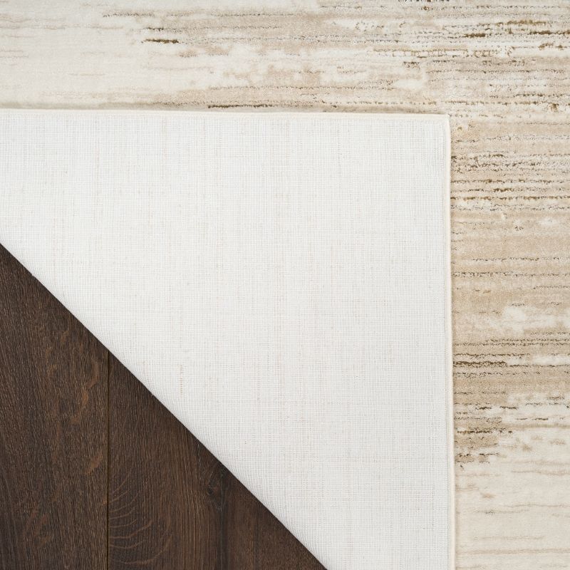 Close-up of a white rug corner on a wooden floor with a textured beige wall.