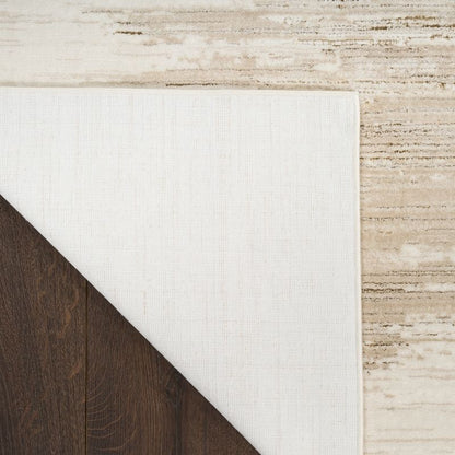 Close-up of a white rug corner on a wooden floor with a textured beige wall.