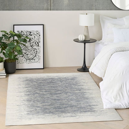 A rectangular area rug with a distressed gray and off-white abstract pattern, styled in a modern bedroom next to a bed and a potted plant.