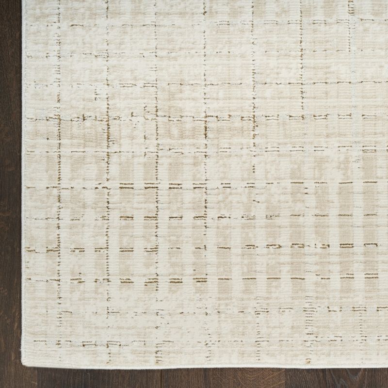 A close-up of a textured area rug with a distressed grid pattern in cream and beige tones, shown on a dark wood floor.
