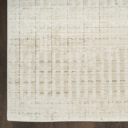 A close-up of a textured area rug with a distressed grid pattern in cream and beige tones, shown on a dark wood floor.