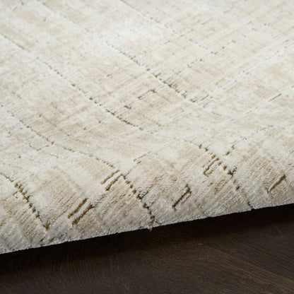 A close-up of a textured area rug in cream and beige with a subtle woven geometric pattern, shown folded over to reveal its underside resting on a dark wood floor.