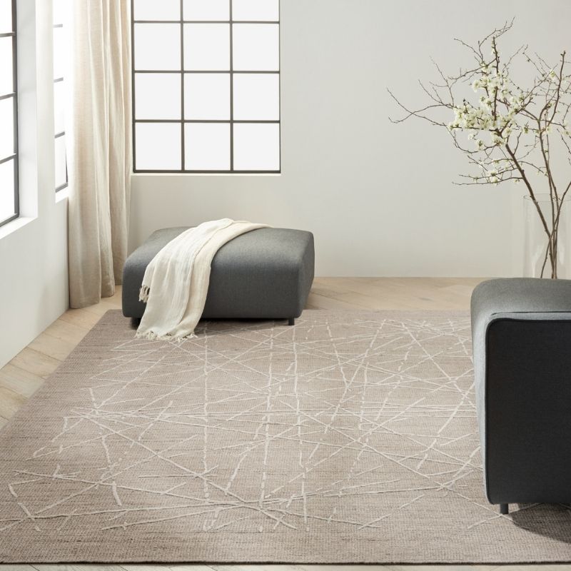 Living room with a patterned rug, gray ottoman, and modern decor.