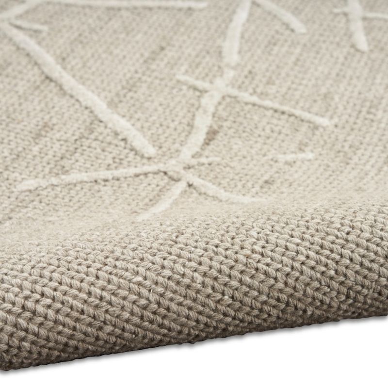 Close-up of a woven rug or textile in a warm light beige/taupe tone with a raised off-white geometric starburst pattern and visible texture.