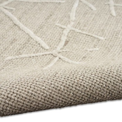 Close-up of a woven rug or textile in a warm light beige/taupe tone with a raised off-white geometric starburst pattern and visible texture.