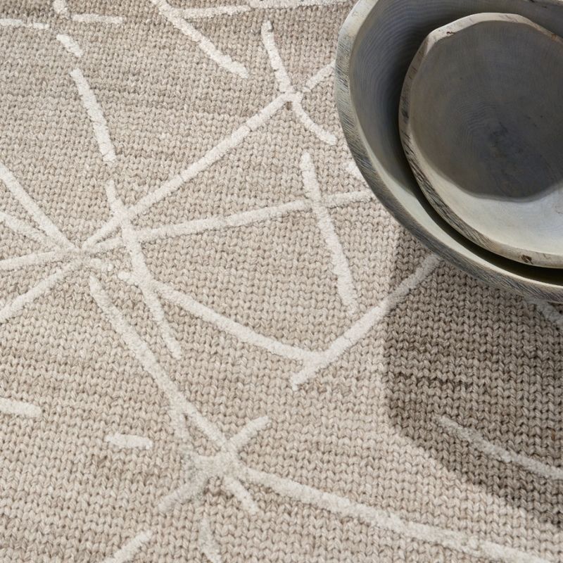 A close-up of a textured beige woven rug with a white geometric starburst pattern, styled with a stack of rustic ceramic bowls in the upper right corner.