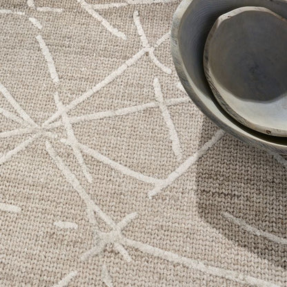 A close-up of a textured beige woven rug with a white geometric starburst pattern, styled with a stack of rustic ceramic bowls in the upper right corner.
