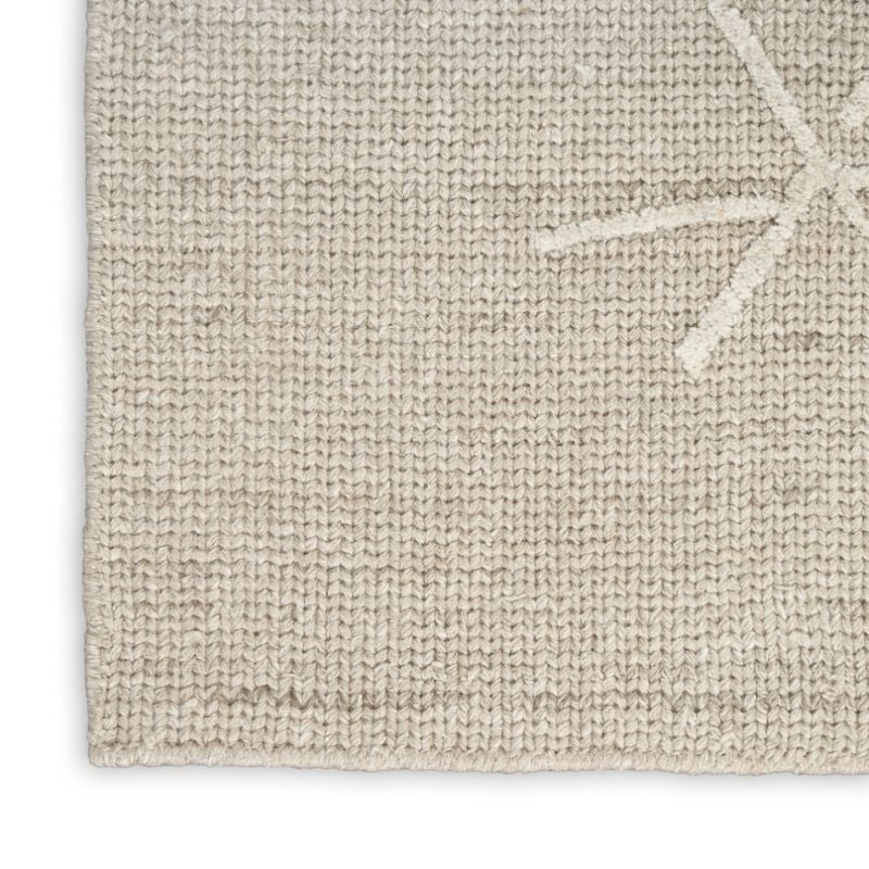 Close-up of a textured woven rug in a light oatmeal beige color, showing the detailed knit pattern and a small portion of a white star motif in the upper right corner.