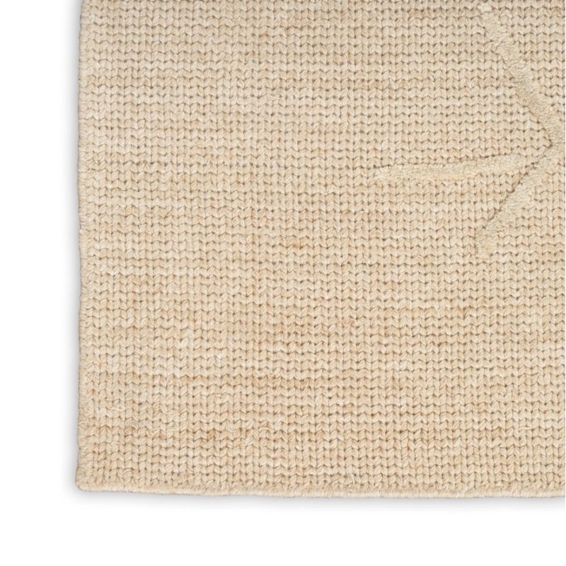 A close-up of a textured woven rug in a natural beige color, showing the detailed knit pattern and folded corner on a white background.