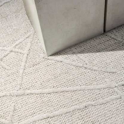 Close-up of a textured off-white woven rug with a geometric linear pattern, shown under the corner of a light gray concrete or stone side table.
