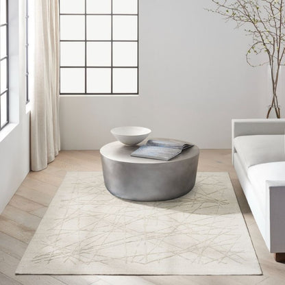 A round gray coffee table in a bright, modern living room setting with a light beige patterned area rug underneath, a white bowl, and a folded magazine on top.