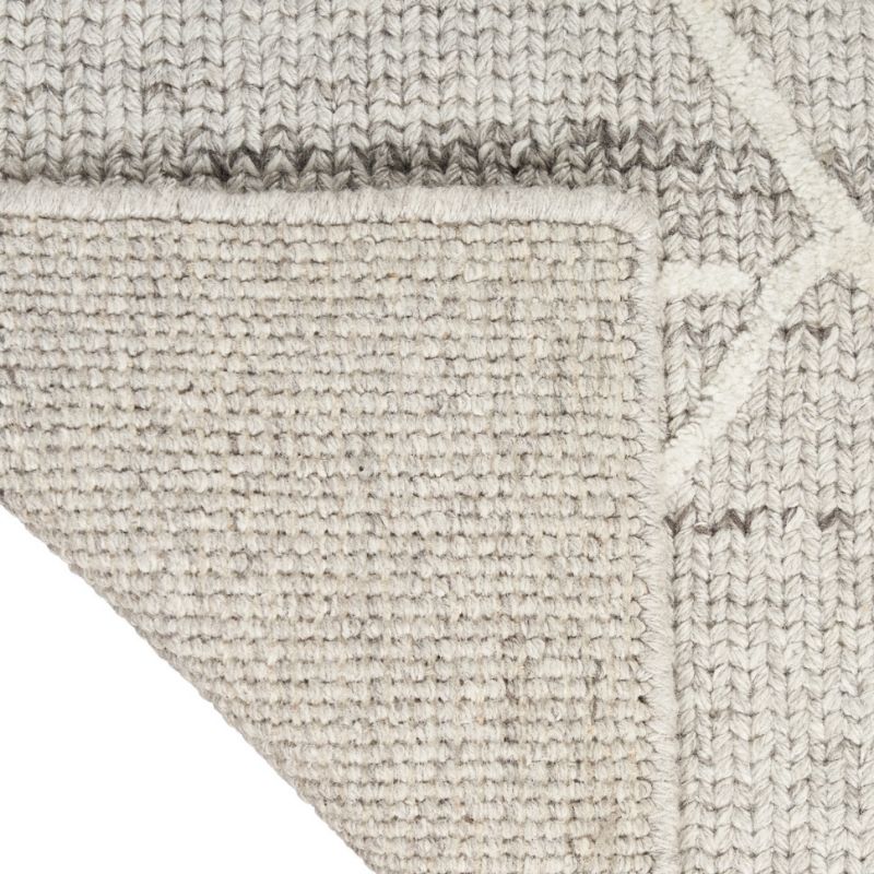 Close-up of a woven area rug showing its textured, heathered light gray and off-white pattern, with a folded corner revealing the underside.