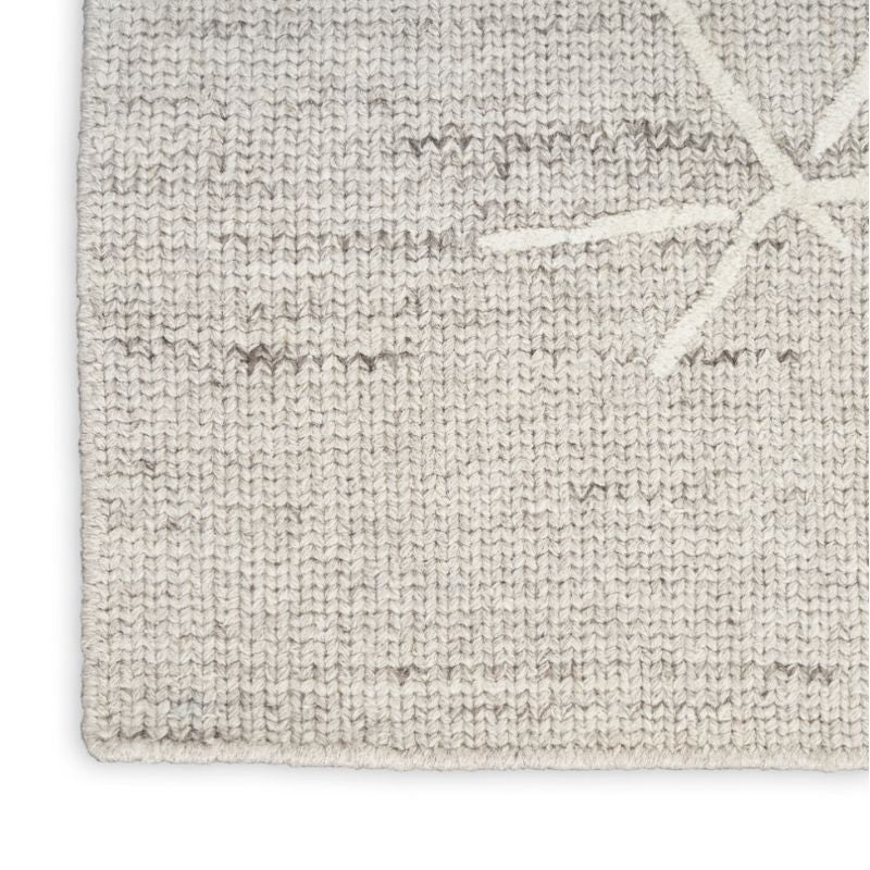 Close-up of a textured woven rug in a light beige and off-white color palette, showing a subtle starburst pattern in the upper right corner.