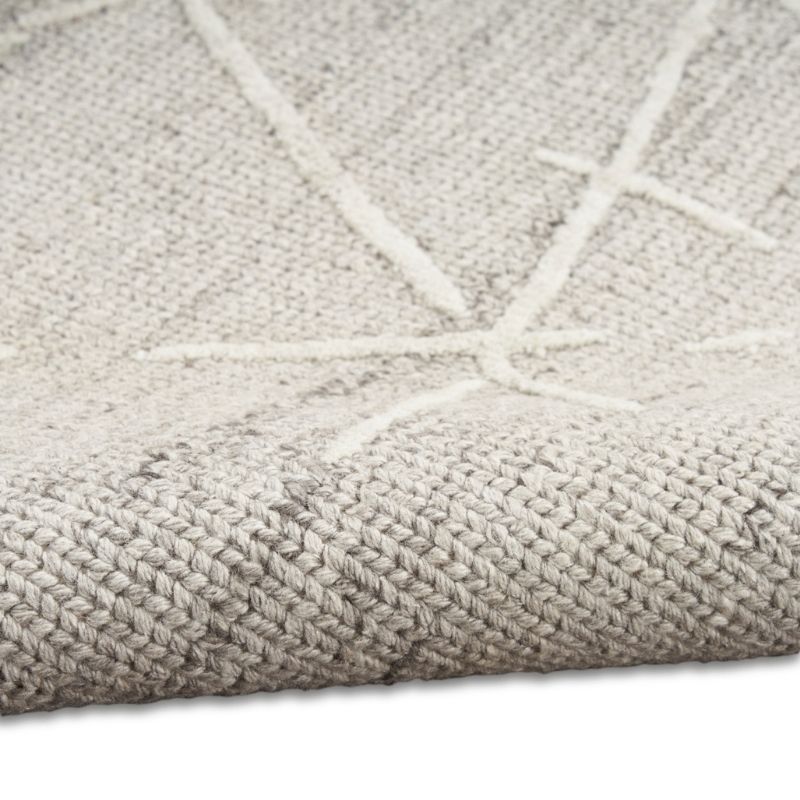 Close-up of a woven rug or textile in a light warm gray-beige tone with a raised cream geometric line pattern, shown folded over on a white background.