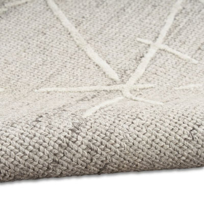Close-up of a woven rug or textile in a light warm gray-beige tone with a raised cream geometric line pattern, shown folded over on a white background.