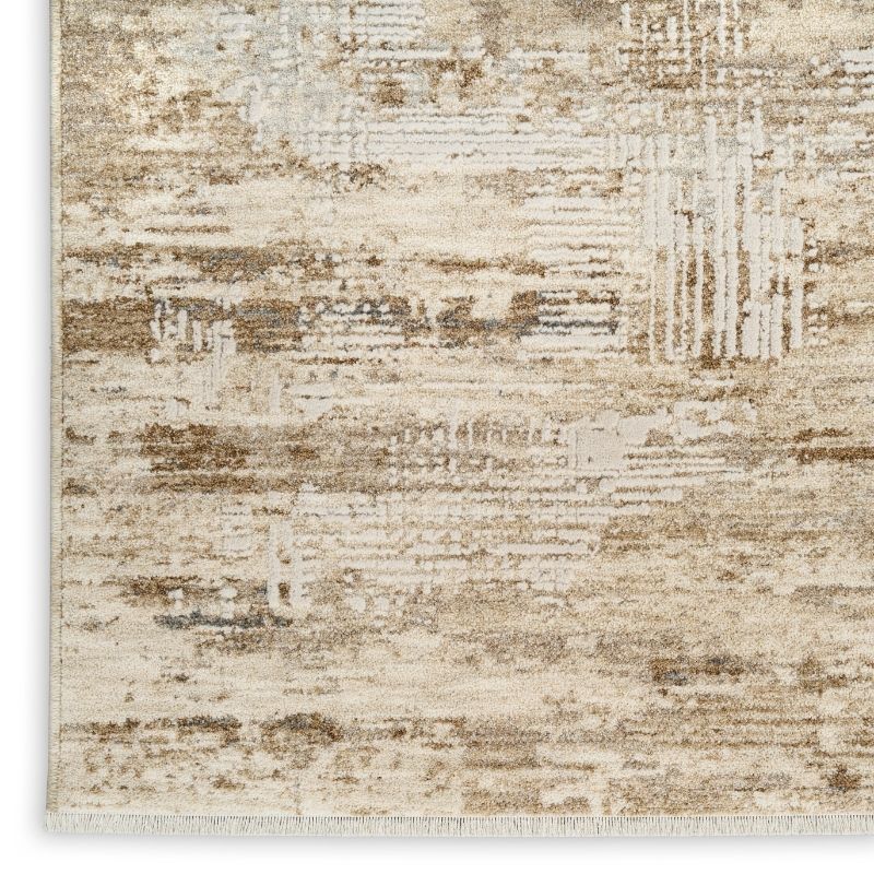 A close-up of a distressed area rug with an abstract, rustic pattern in beige, cream, and light brown tones, showing the texture and fringe on one side.