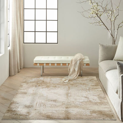 A rectangular area rug with a distressed, abstract pattern in beige, cream, and light brown tones, styled in a bright, modern living room next to a sofa and a bench.