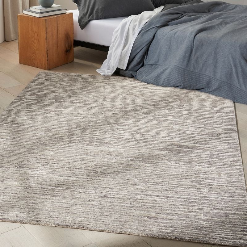 Gray textured rug in a bedroom setting with a bed and wooden nightstand.