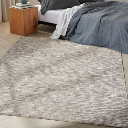 Gray textured rug in a bedroom setting with a bed and wooden nightstand.